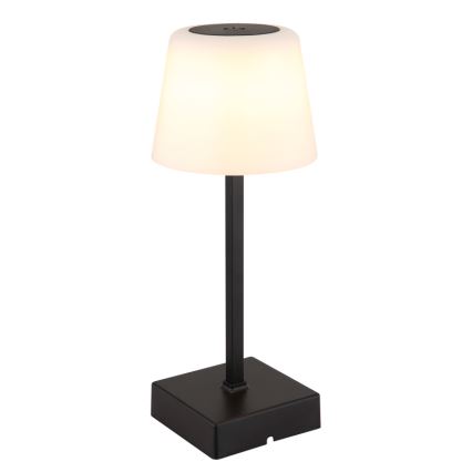 Stolová lampa svieti. Má biely, kužeľovitý tienidlo a čierny kovový stojan s štvorcovou základňou. Lampa je osvetlená.