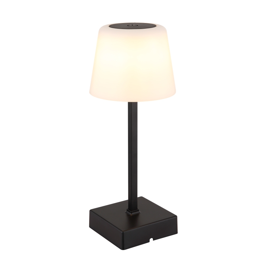 Stolová lampa svieti. Má biely, kužeľovitý tienidlo a čierny kovový stojan s štvorcovou základňou. Lampa je osvetlená.