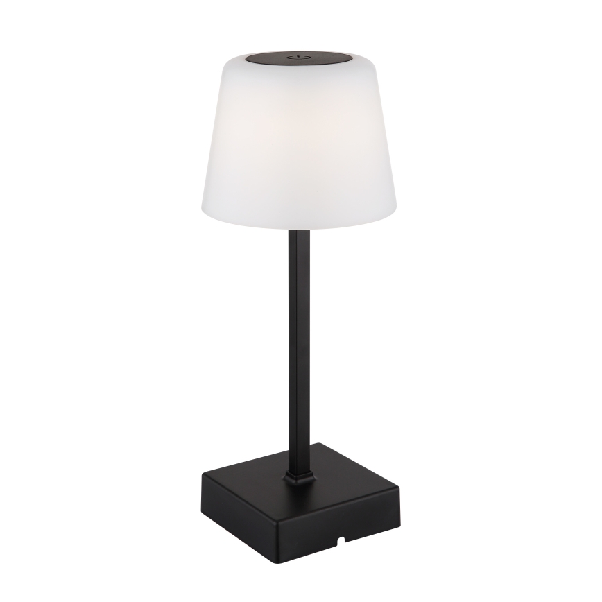 Stolná lampa s bielym tienidlom a čiernym podstavcom svieti. Tienidlo je valcovité, podstavec štvorcový. Lampa je umiestnená na bielom pozadí.