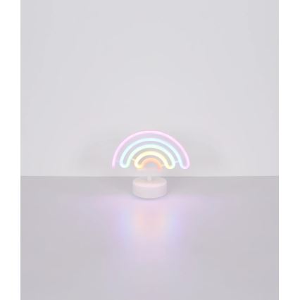 Neonová lampa v tvare dúhy svieti na svetlom podklade. Svetlo dúhy je viacfarebné, svietiace a je umiestnené na malej bielej základni.