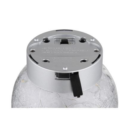 Strieborný kryt s vypínačom a nápisom „Use Rechargeable Battery Only. Similar Replacement R/R. Use Same Battery Rechargeable.“ je na sklenenej guľovej lampe. Na kryte je aj nápis „Made in China“.