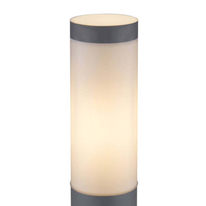 Svietidlo svieti. Valcový tvar, sivý podstavec a mliečne biely difúzor. Izolované biele pozadie.