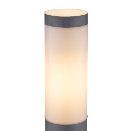 Valcovitá lampa svieti. Svetlo presvitá mliečnym difúzorom. Spodná a vrchná časť sú sivé.