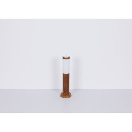 Záhradné svietidlo stojí na svetlej podlahe. Svietidlo je valcovité, hnedé drevené s bielym difúzorom. Svietidlo je umiestnené v jednoduchom, bielom prostredí.