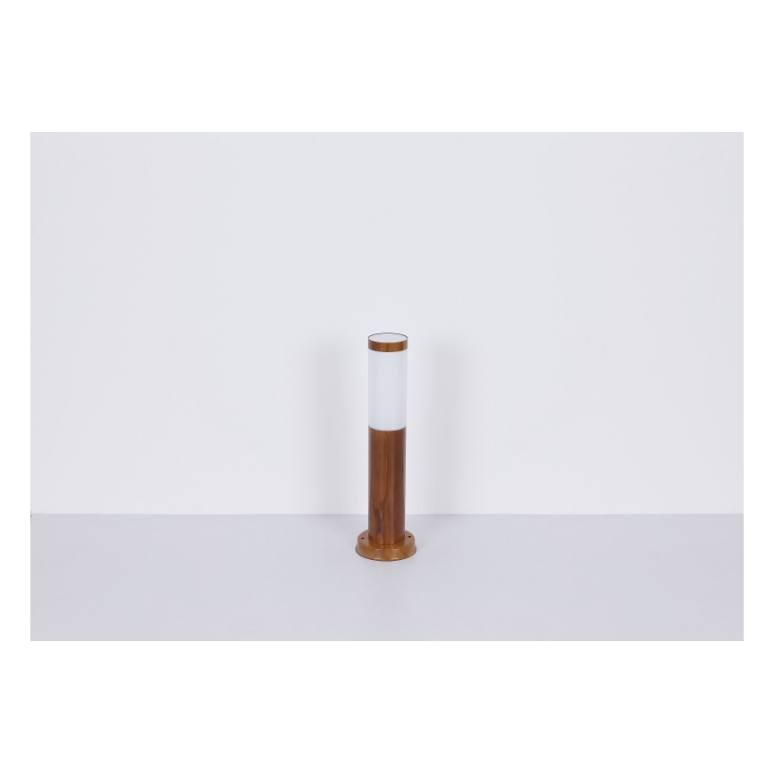 Záhradné svietidlo stojí na svetlej podlahe. Svietidlo je valcovité, hnedé drevené s bielym difúzorom. Svietidlo je umiestnené v jednoduchom, bielom prostredí.