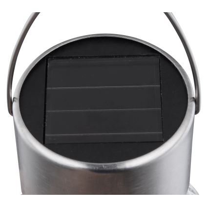 Solárny panel absorbuje svetlo. Je umiestnený na vrchu kovovej nádoby s úchytkou. Nádoba vyzerá ako lampa.