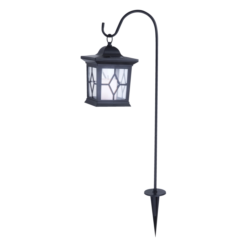 Solárna lampa visí na zahradnom stojane. Stojan je zasadený do zeme. Lampa je štvorcového tvaru s mliečnym sklom.