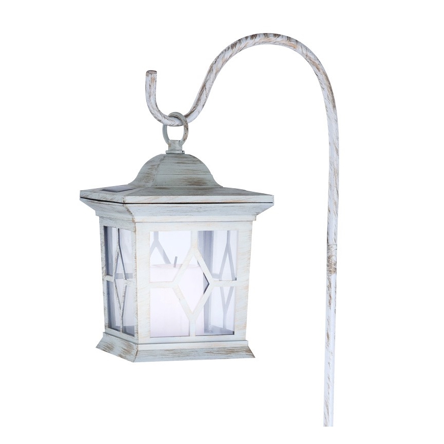 Solárna lampa visí na zahradnom stojane. Lampa je svetlomodrá, štvorcová, s ozdobnými oknami a imitáciou sviečky vo vnútri. Stojan je kovový, zakrivený, svetlomodrej farby.