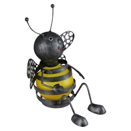 Kovová soška včely sedí na bielom pozadí. Včela je sivá s žltým bruškom z kovového drôtu. Jej nohy a tykadlá sú kovové.