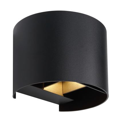 Čierna nástenná lampa s dvoma zlatými LED svetlami svieti. Lampa je valcového tvaru, čiastočne zakrivená. Je umiestnená na bielom pozadí.