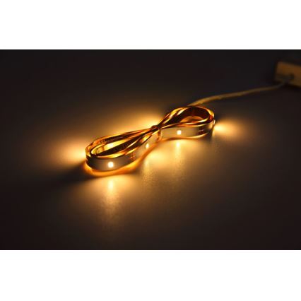 LED pásik svieti na tmavom povrchu. Je stočený do tvaru osmičky. Pripojený je k tenkému káblu.