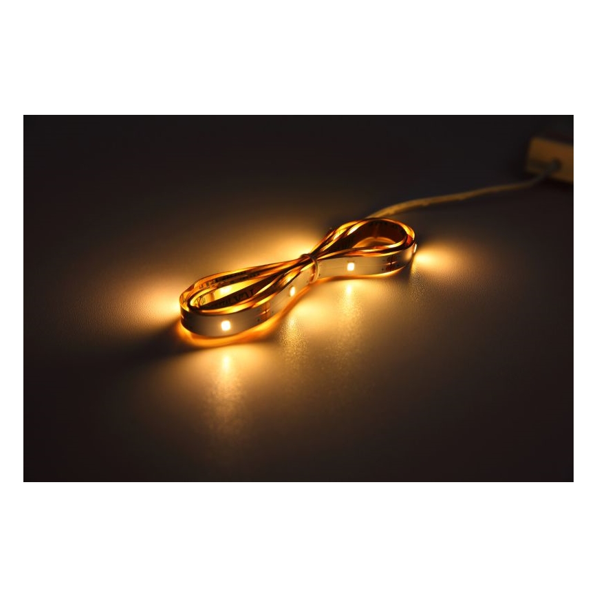 LED pásik svieti na tmavom povrchu. Je stočený do tvaru osmičky. Pripojený je k tenkému káblu.