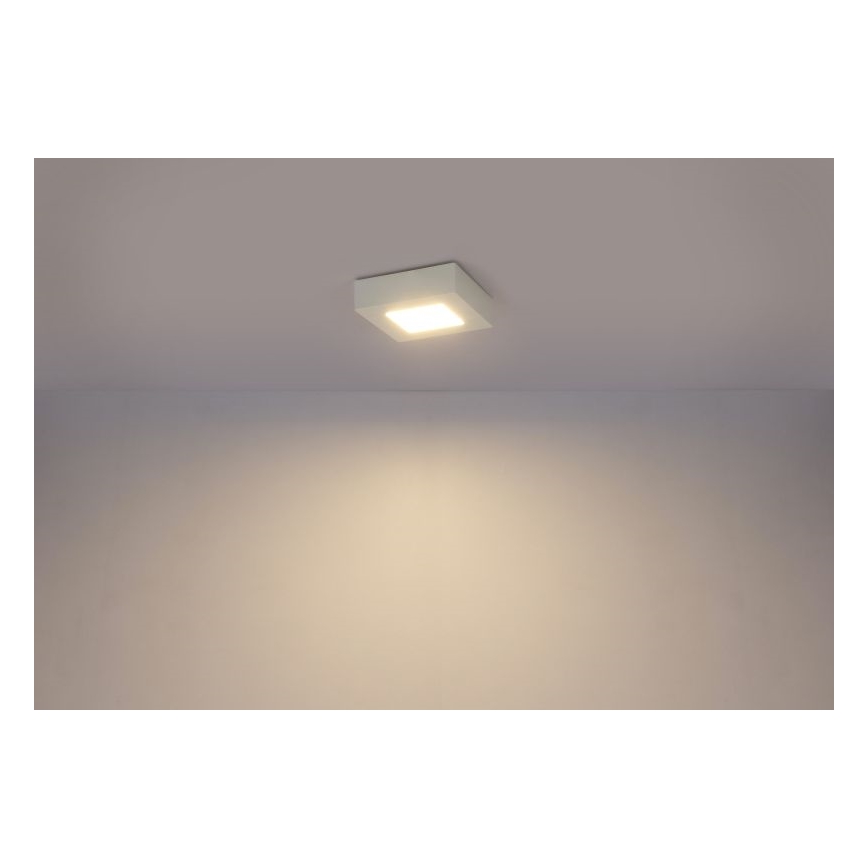 Štvorcové svietidlo svieti na svetlohnedom strope. Svietidlo je zapustené do stropu. Steny sú svetlohnedé.