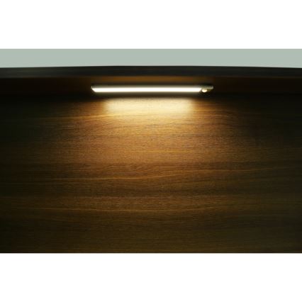 Svetlo diódová LED lampa svieti na tmavohnedý drevený povrch. Lampa je pripevnená k hornej časti povrchu. Svetlo vytvára zreteľný svetelný kužeľ.