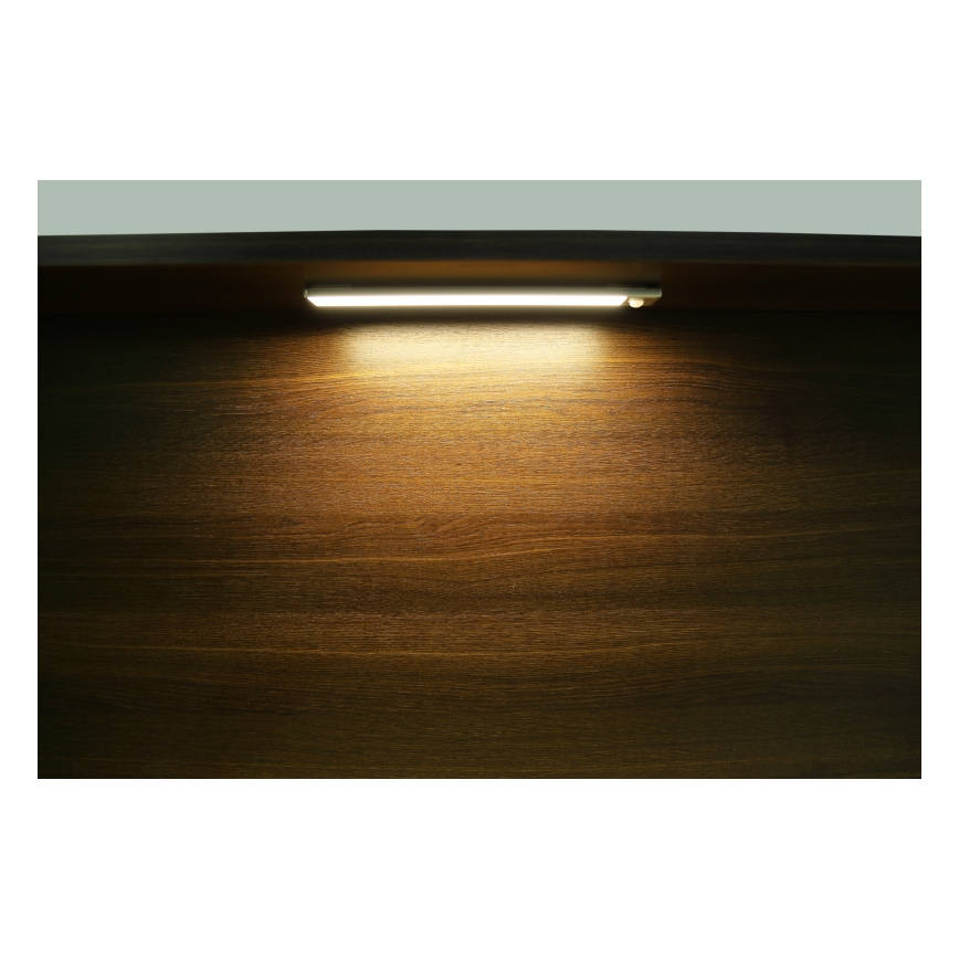 Svetlo diódová LED lampa svieti na tmavohnedý drevený povrch. Lampa je pripevnená k hornej časti povrchu. Svetlo vytvára zreteľný svetelný kužeľ.