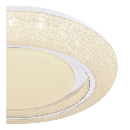 Svietidlo svieti. Jeho oválny tvar má vrstvený dizajn s pieskovou štruktúrou vonkajšieho kruhu a svetložltým vnútorným difúzorom. Je umiestnené na bielom pozadí.