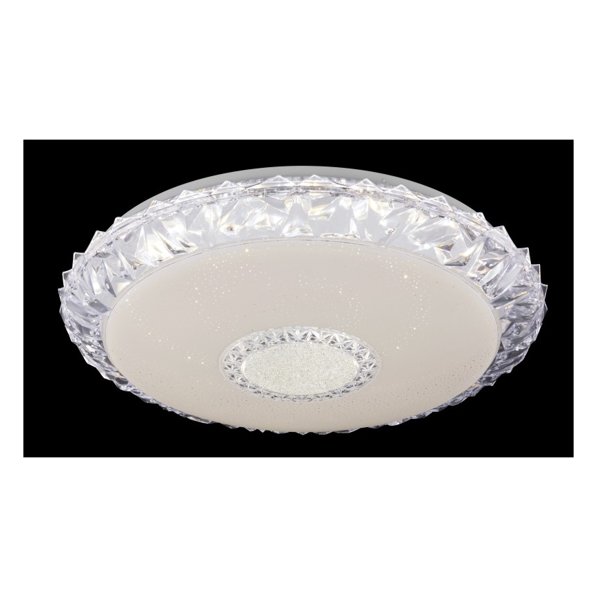 Svetlo svieti na tmavom pozadí. Je to ploché, okrúhle LED svietidlo s kryštálovým okrajom a krémovým stredom posiatym drobnými bodkami svetla. Stred obsahuje ďalší menší kruh s kryštálmi.