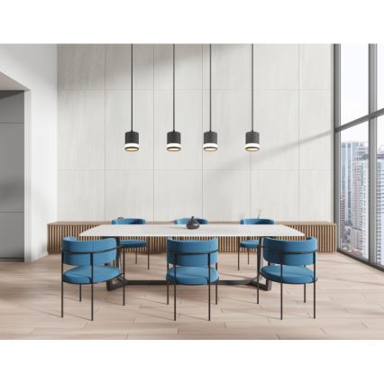 Dlhý biely jedálenský stôl s modrými stoličkami je umiestnený v moderne zariadenej miestnosti s drevenou podlahou a veľkým oknom s výhľadom na mesto. Nad stolom visia štyri čierne závesné lampy.