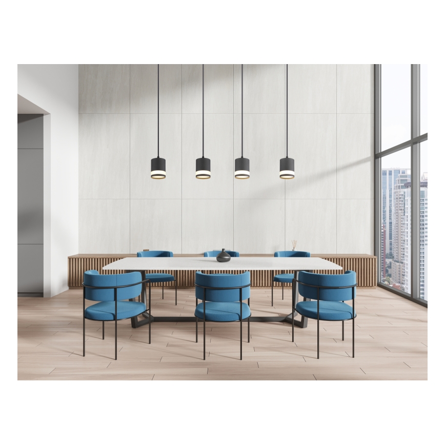 Dlhý biely jedálenský stôl s modrými stoličkami je umiestnený v moderne zariadenej miestnosti s drevenou podlahou a veľkým oknom s výhľadom na mesto. Nad stolom visia štyri čierne závesné lampy.
