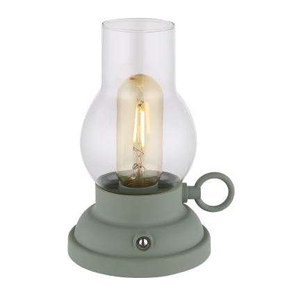 Stolová lampa svieti. Je zložená zo zelenej kovovej základne, skleneného tienidla a LED žiarovky s vláknom. Na základni je vypínač.