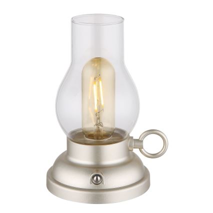 Stolová lampa svieti. Je vyrobená z kovu v svetlo šampanskom odtieni a má sklenený tienidlo v tvare fľaše. Má malý vypínač na spodnej časti.