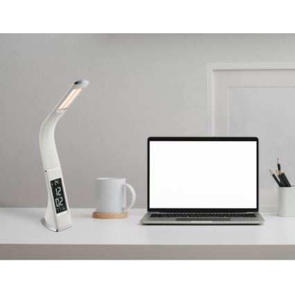 Stolová lampa s digitálnym budíkom svieti na bielom stole. Vedľa nej je notebook a hrnček. Na displeji lampy je zobrazené: 24|12 02.