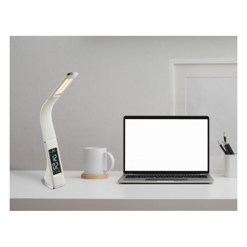 Stolová lampa s digitálnym budíkom svieti na bielom stole. Vedľa nej je notebook a hrnček. Na displeji lampy je zobrazené: 24|12 02.