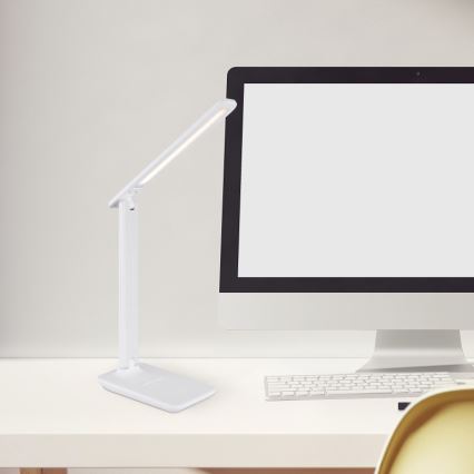 Biela stolová lampa s LED osvetlením svieti na bielom stole vedľa počítača a klávesnice.