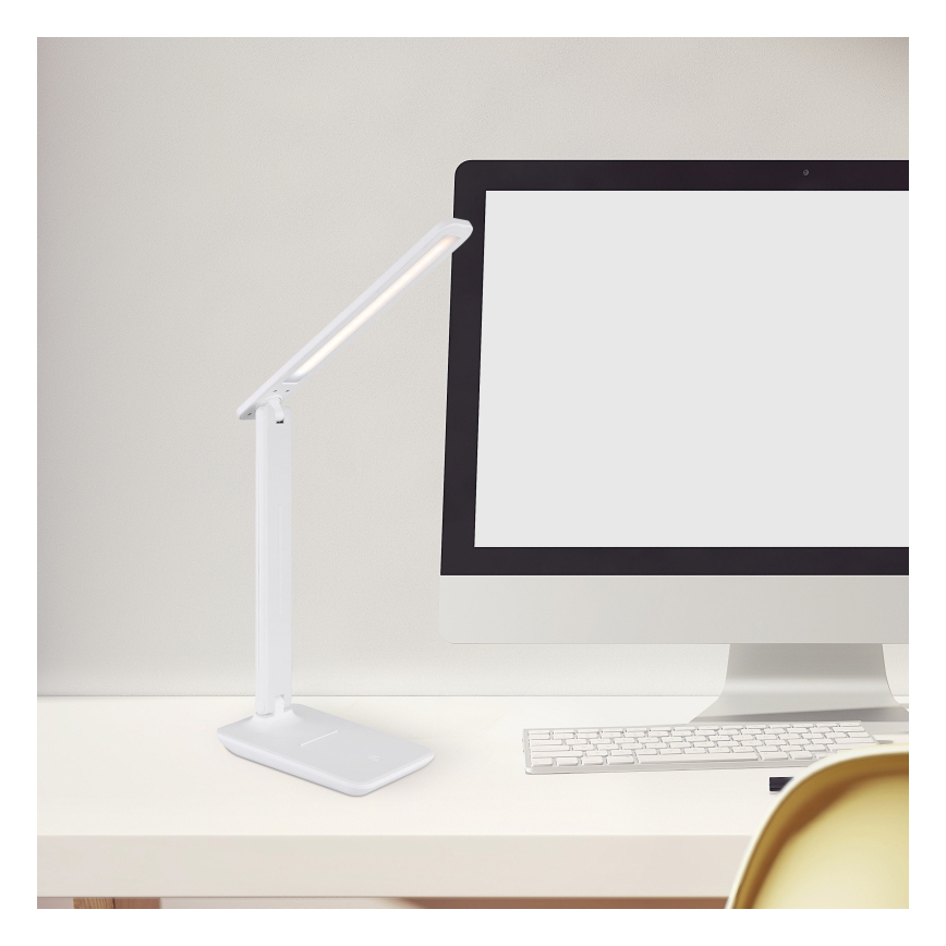 Biela stolová lampa s LED osvetlením svieti na bielom stole vedľa počítača a klávesnice.