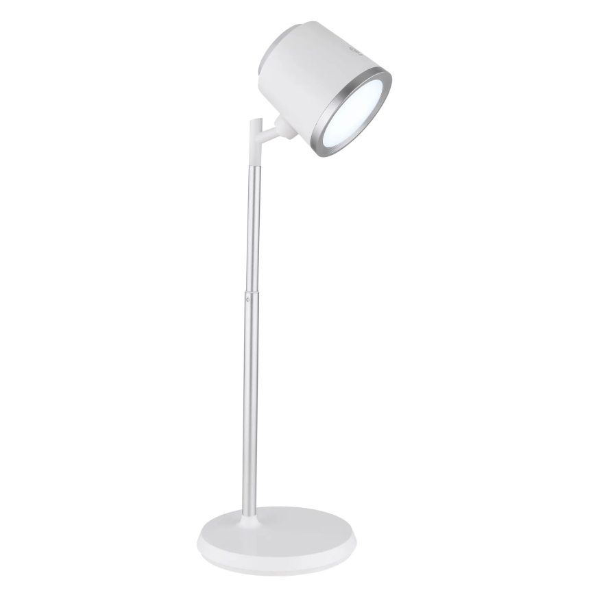 Stolová lampa s bielym tienidlom a strieborným stojanom svieti. Je umiestnená na bielom podstavci na bielom pozadí.