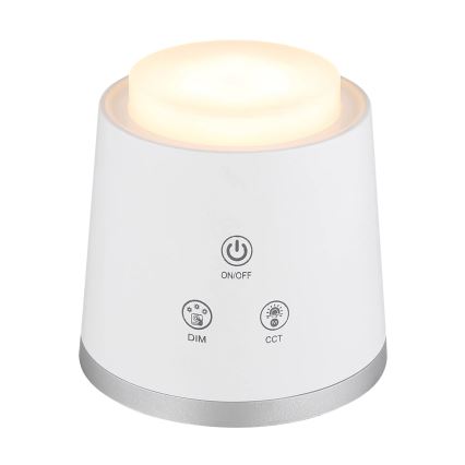 Biela stolová lampa svieti. Na spodnej časti sú tlačidlá: ON/OFF, DIM, CCT. Lampa má strieborný okraj.