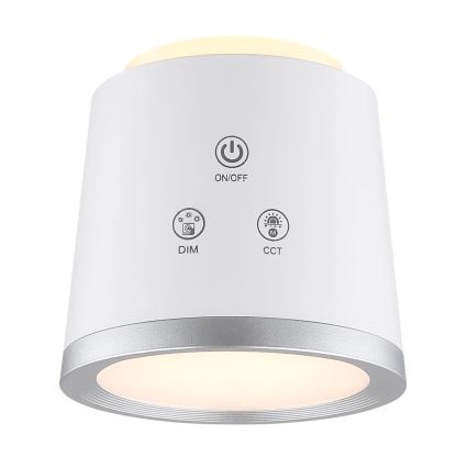 Biela guľatá lampa svieti. Na jej povrchu sú tlačidlá: ON/OFF, DIM, CCT. Lampa má strieborný okraj.