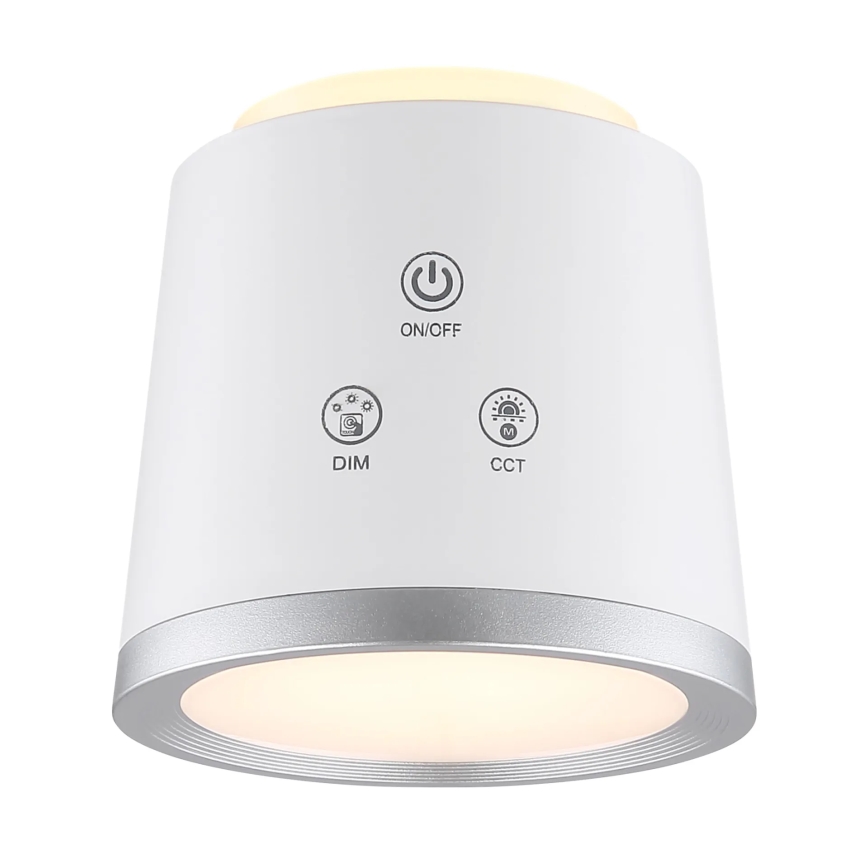 Biela guľatá lampa svieti. Na jej povrchu sú tlačidlá: ON/OFF, DIM, CCT. Lampa má strieborný okraj.