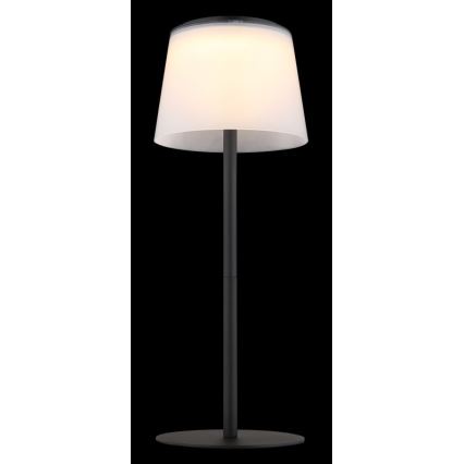 Stolová lampa svieti. Má biely tienidlo a čierny kovový stojan s okrúhlou základňou. Je umiestnená na tmavom pozadí.
