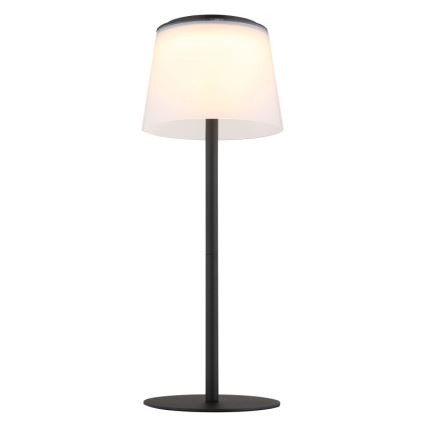 Stojacia lampa svieti. Má vysoký, čierny stojan a valcový tienidlo z mliečneho skla. Lampa stojí na kruhovej základni.