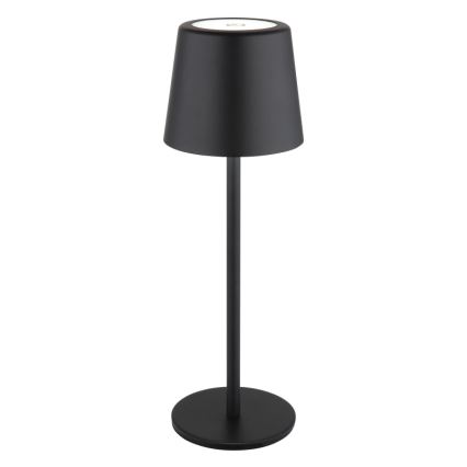 Čierna stolová lampa s valcovým tienidlom svieti. Má vysokú, úzku nohu a kruhovú základňu. Lampa je umiestnená na bielom pozadí.