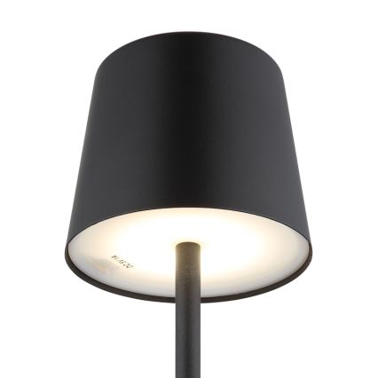 Stolová lampa s čiernym tienidlom kužeľovitého tvaru svieti. Vnútorná časť tienidla je biela a presvitá svetlo. Na spodnej strane tienidla je viditeľný text „24 15 24“.