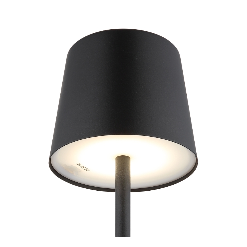 Stolová lampa s čiernym tienidlom kužeľovitého tvaru svieti. Vnútorná časť tienidla je biela a presvitá svetlo. Na spodnej strane tienidla je viditeľný text „24 15 24“.