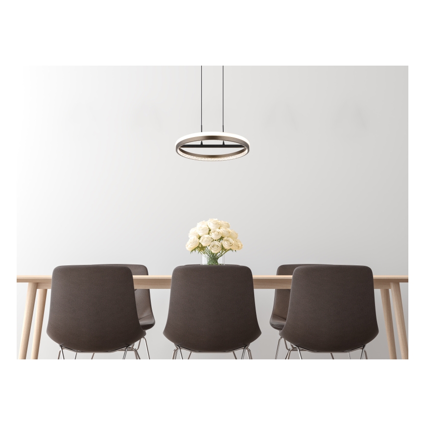 Kruhový závesný luster s LED osvetlením visí nad jedálenským stolom s hnedými stoličkami. Na stole je váza s bielymi ružami.