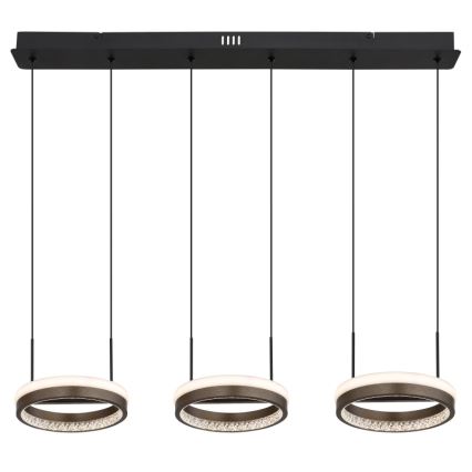 Trojdielne LED svietidlo visí z čiernej lišty. Každá kruhová lampa má vnútorný svetelný prstenec a vonkajší okraj posiaty kryštálikmi. Svietidlo je zavesené na čiernych kábloch.