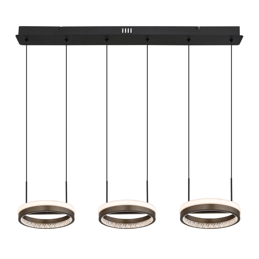 Trojdielne LED svietidlo visí z čiernej lišty. Každá kruhová lampa má vnútorný svetelný prstenec a vonkajší okraj posiaty kryštálikmi. Svietidlo je zavesené na čiernych kábloch.