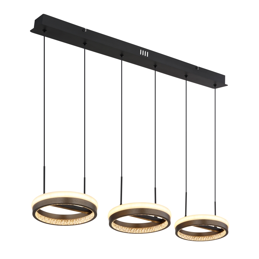 Trojité kruhové LED svietidlo visí z čiernej stropnej lišty. Každé svietidlo je tvorené vonkajším kruhom z mliečneho materiálu, vnútorným kruhom z tmavého kovu a zdobené kryštálikmi.