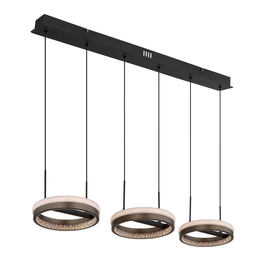 Trojramenné závesné svietidlo visí z čiernej lišty. Každá lampa má kruhový tvar s vnútorným tmavohnedým prstencom obklopeným kryštálmi a vonkajším mliečnobielym prstencom.