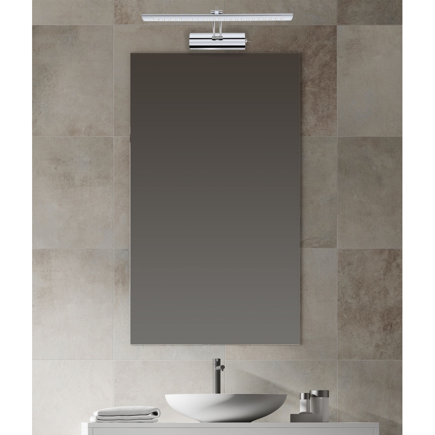 Svetlo nad zrkadlom svieti v kúpeľni. Zrkadlo je obdĺžnikové, umiestnené nad umývadlom. Kúpeľňa má dlaždicovú stenu.