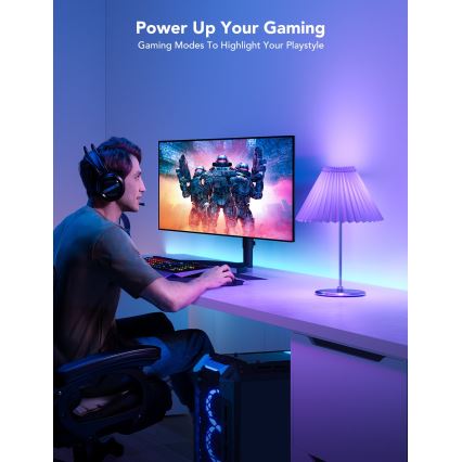 Muž hrá hru na počítači s hernými slúchadlami. Svetlo z farebných LED pásikov a stolovej lampy osvetľuje stôl a priestor. Text na obrázku znie: „Power Up Your Gaming. Gaming Modes To Highlight Your Playstyle.“