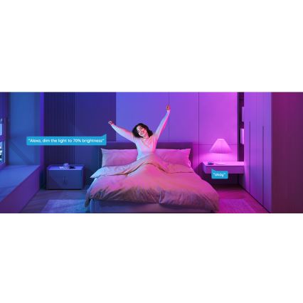 Žena v posteli dvíha ruky. Svetlo v spálni je tlmené na 70% jasu hlasovým ovládaním: „Alexa, zníž svetlo na 70% jasu.“ Systém odpovedá: „Okay“.