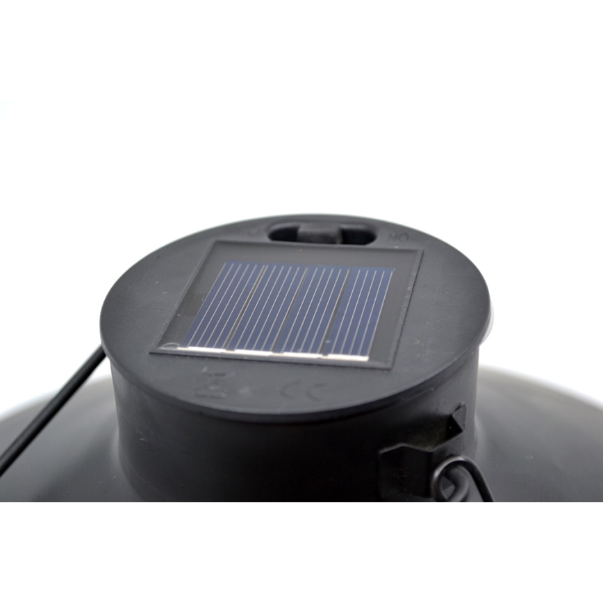 Solárny panel nabíja solárnu lampu. Panel je umiestnený na vrchu čiernej, okrúhlej lampy. Na panely sú viditeľné symboly CE.