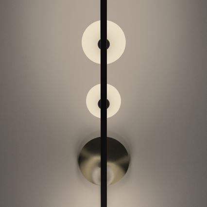 Svietidlo s tromi kruhovými svetlami pripevnené na vertikálnej tyči svieti na svetlosivej stene. Dve horné svetlá sú biele, spodné je kovové a odráža svetlo.