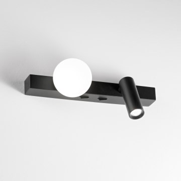 Dvojité nástenné svietidlo svieti. Jedna časť je guľovitá matná biela, druhá je valcovitá s bodovým svetlom, obe sú upevnené na čiernej lište. Svietidlo je na bielom pozadí.