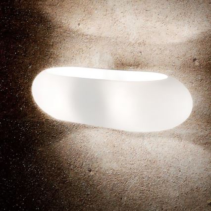Oválna biela lampa svieti na betónovej stene. Lampa je zapustená do steny. Svetlo vyžaruje z vnútra lampy.
